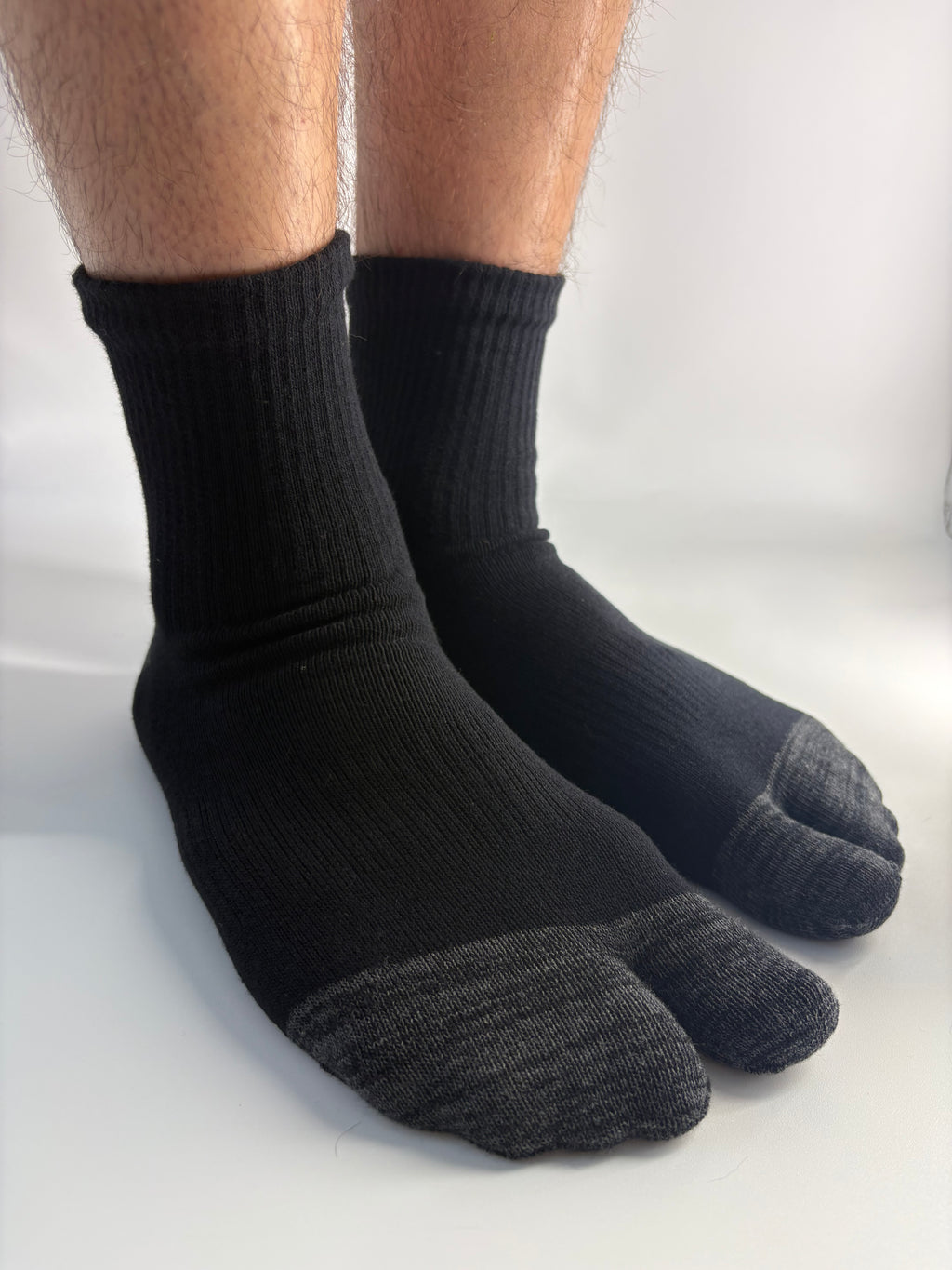 A pair of black tabi socks worn on a person's feet, shown against a plain white studio background.