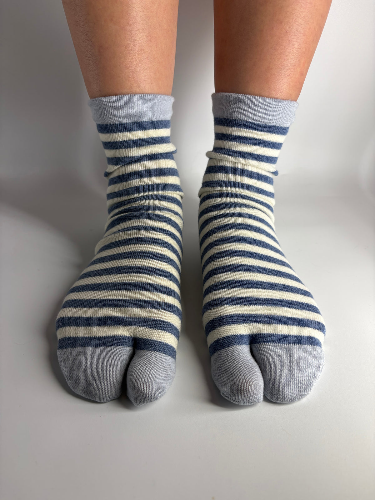 a person wearing nay and cream striped tabi split toe socks on a white background