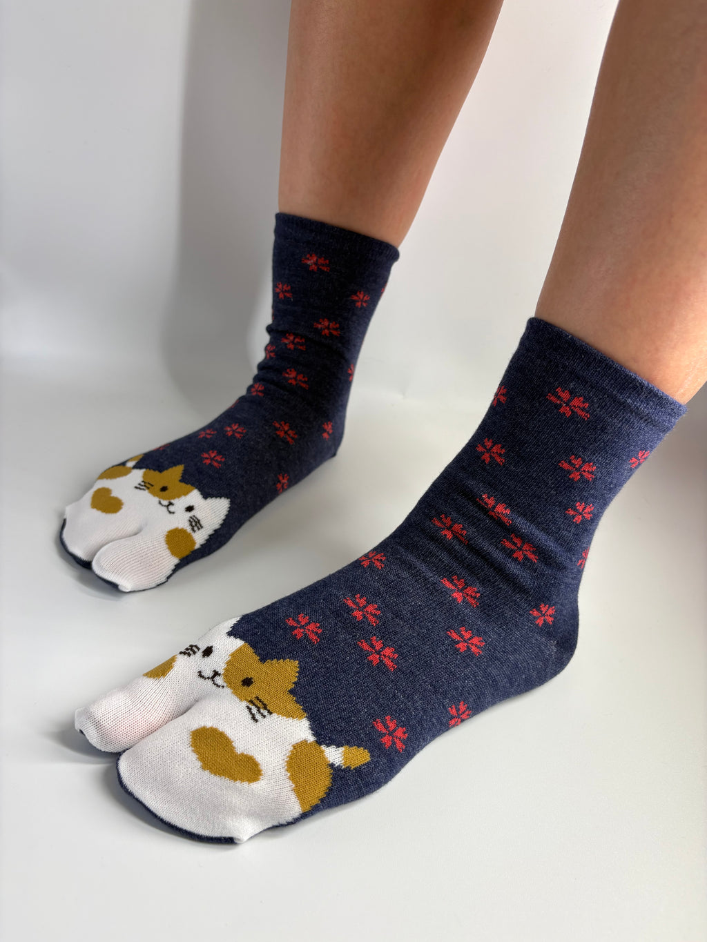 A pair of navy blue socks with a pattern of small red flowers and cat faces on the toes, worn on feet resting on a white surface.