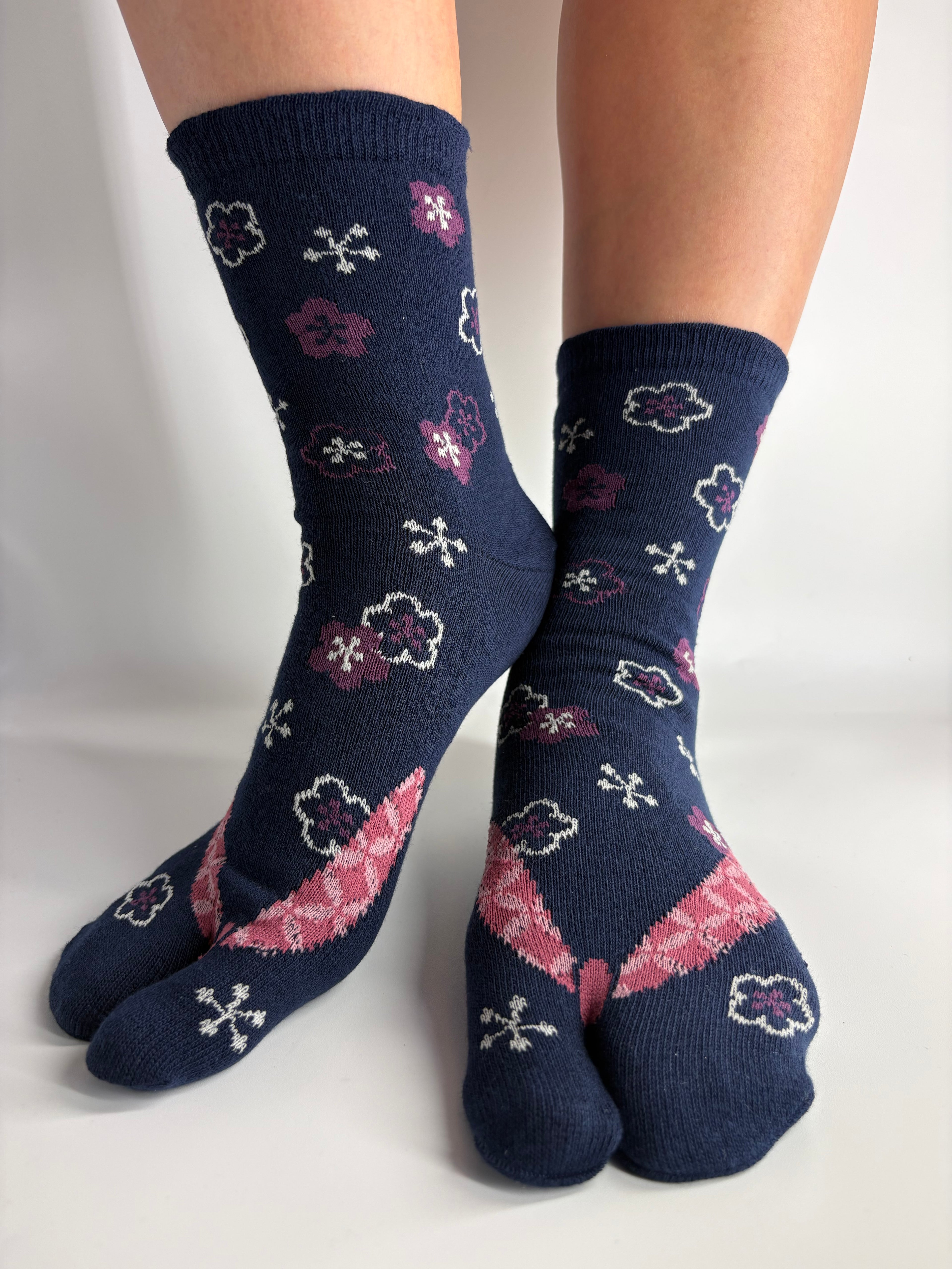A pair of navy blue toe socks with pink and purple floral patterns, shown on feet against a plain white background.
