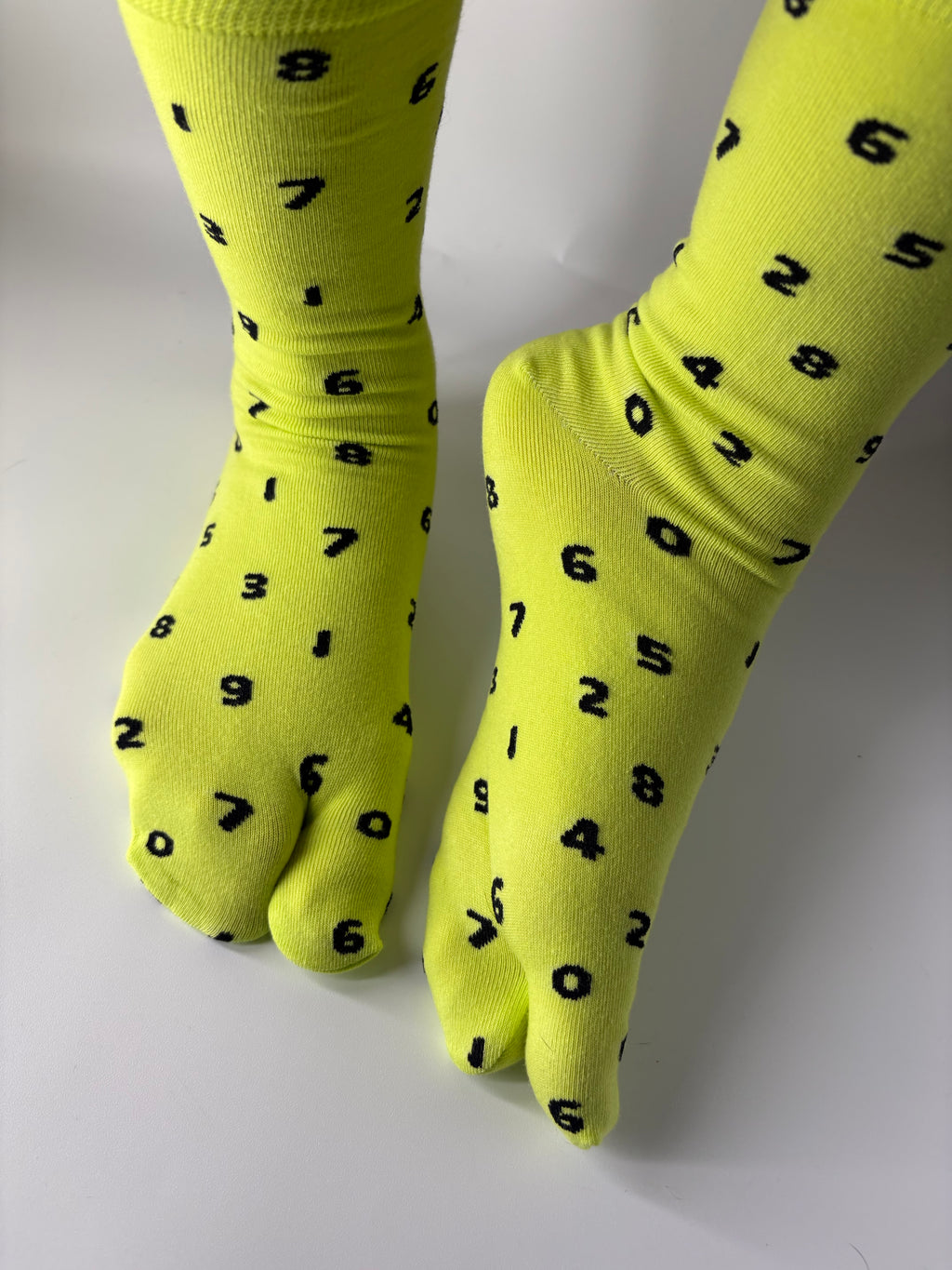 Tabi Co. neon yellow split toe cotton socks with a scattered black number print, worn on feet