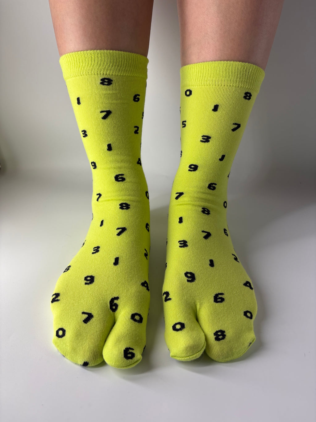 Tabi Co. neon yellow split toe cotton socks with a scattered black number print, worn on feet