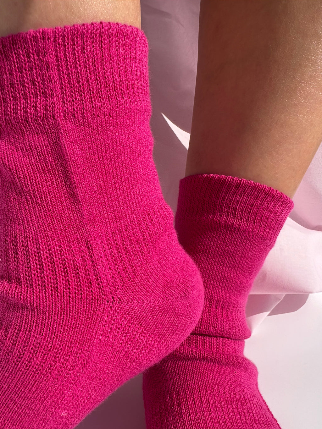 Bright pink cotton quarter socks worn on feet, shown in a close-up shot with a soft pink background.