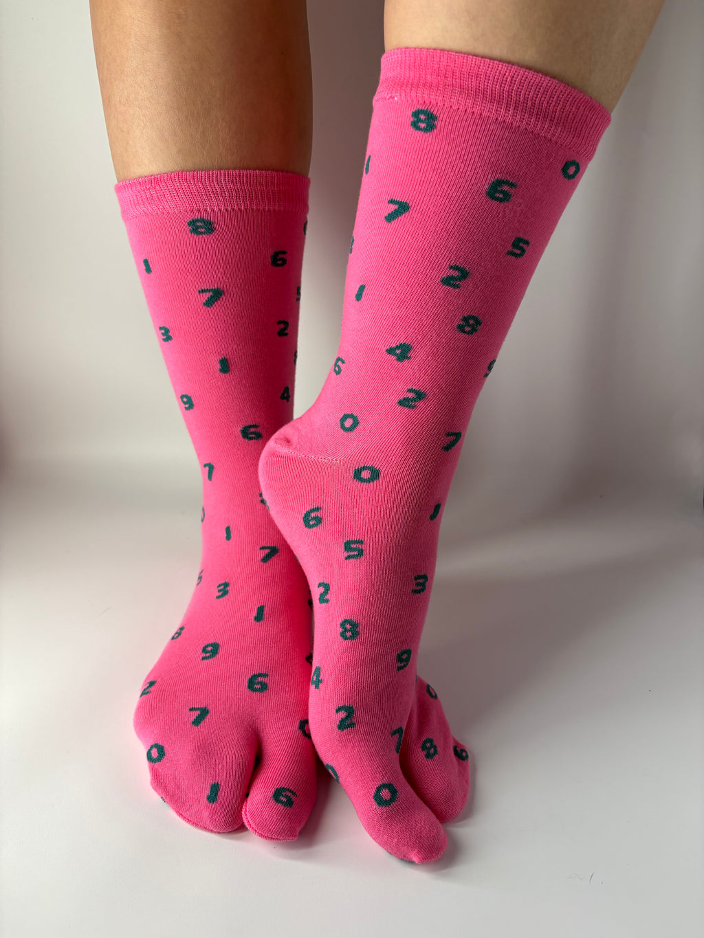 Tabi Co. pink split-toe cotton socks with a scattered green number print, worn on feet