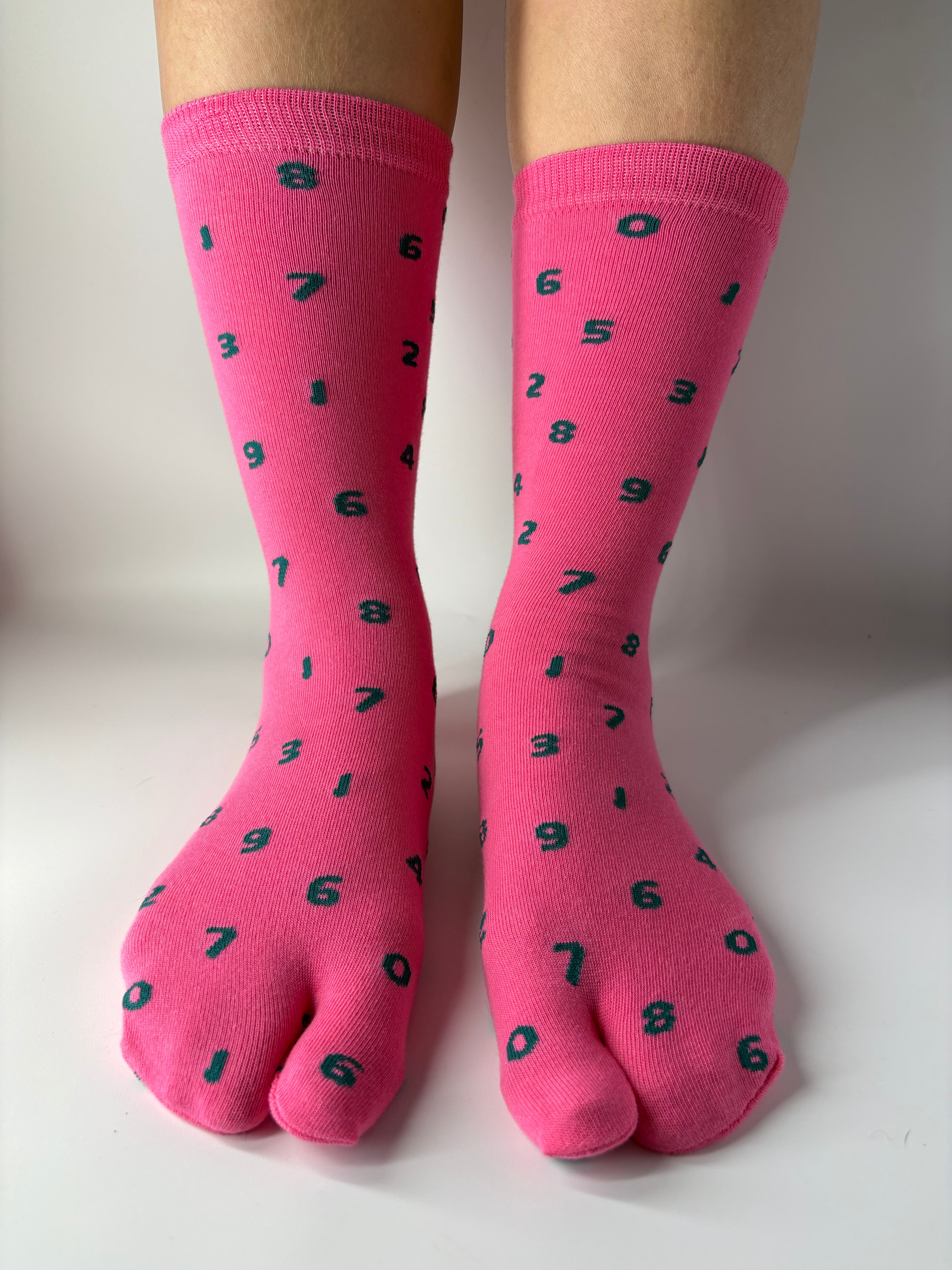 Tabi Co. pink split-toe cotton socks with a scattered green number print, worn on feet