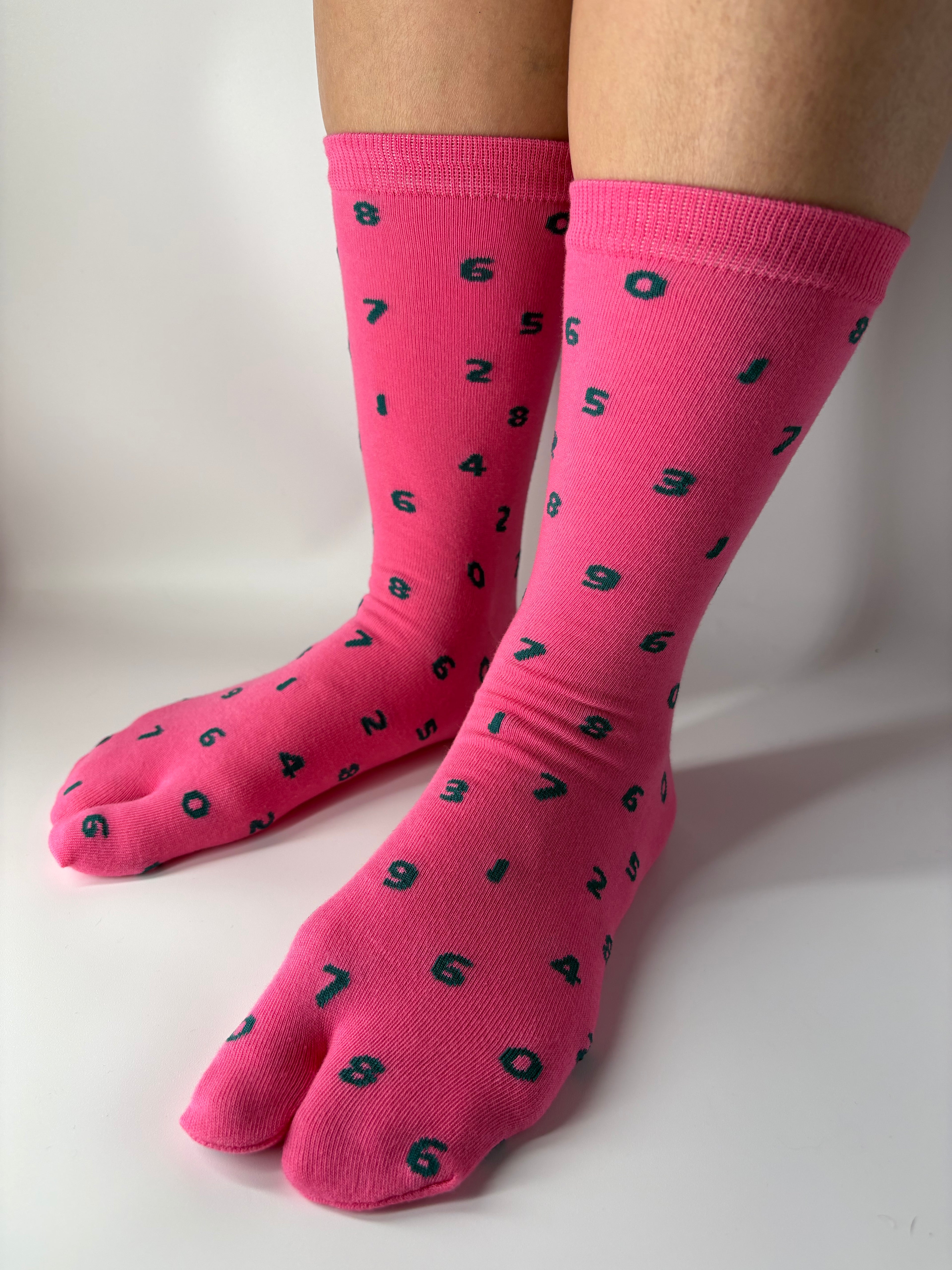 Tabi Co. pink split-toe cotton socks with a scattered green number print, worn on feet