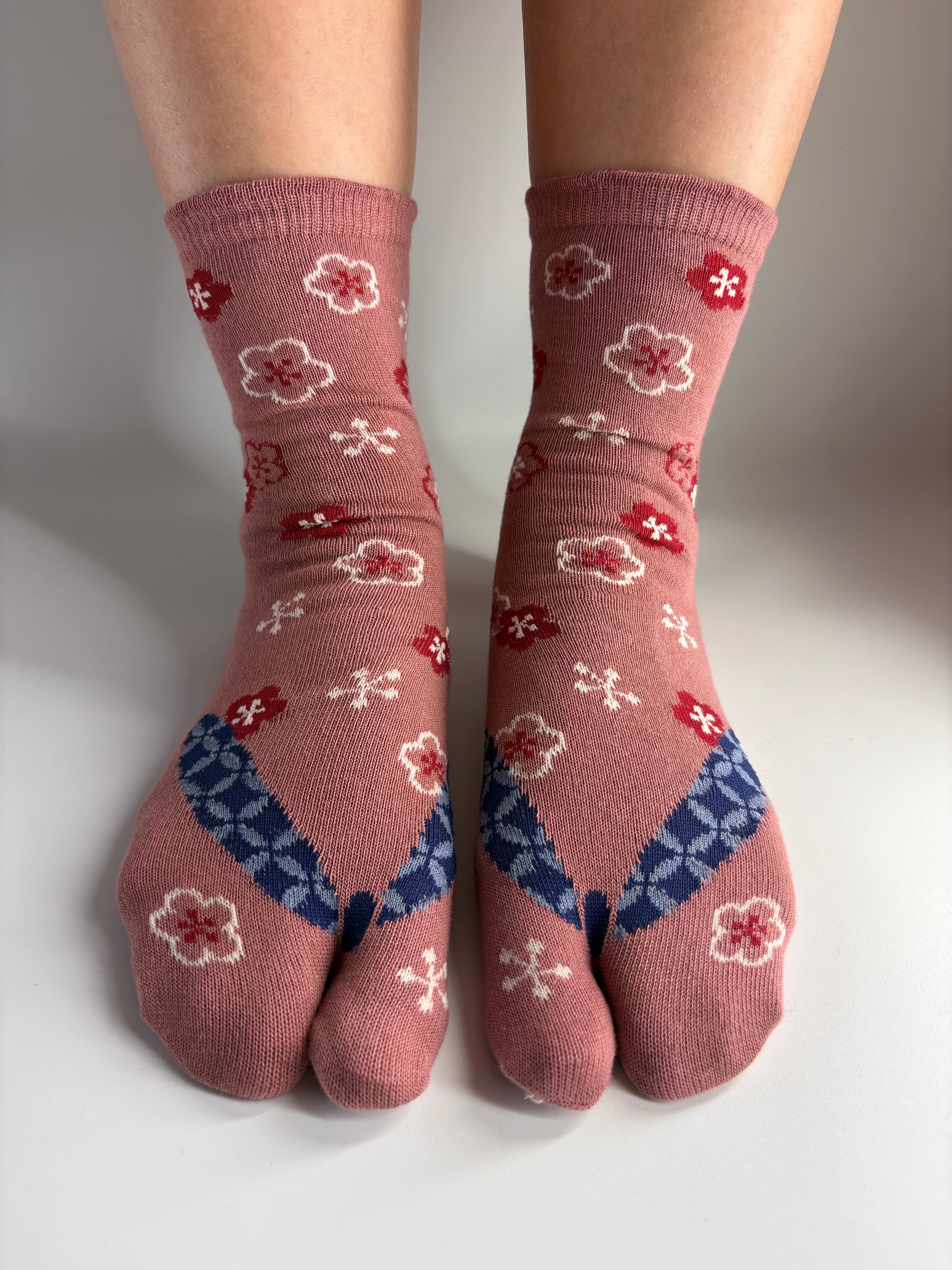 A pair of pink japanese tabi socks with blue and white geometric patterns and small red and white floral motifs, shown on feet against a plain light background.
