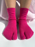 Bright pink tabi socks worn on a person's feet, shown against a white surface with light pink fabric in the background.