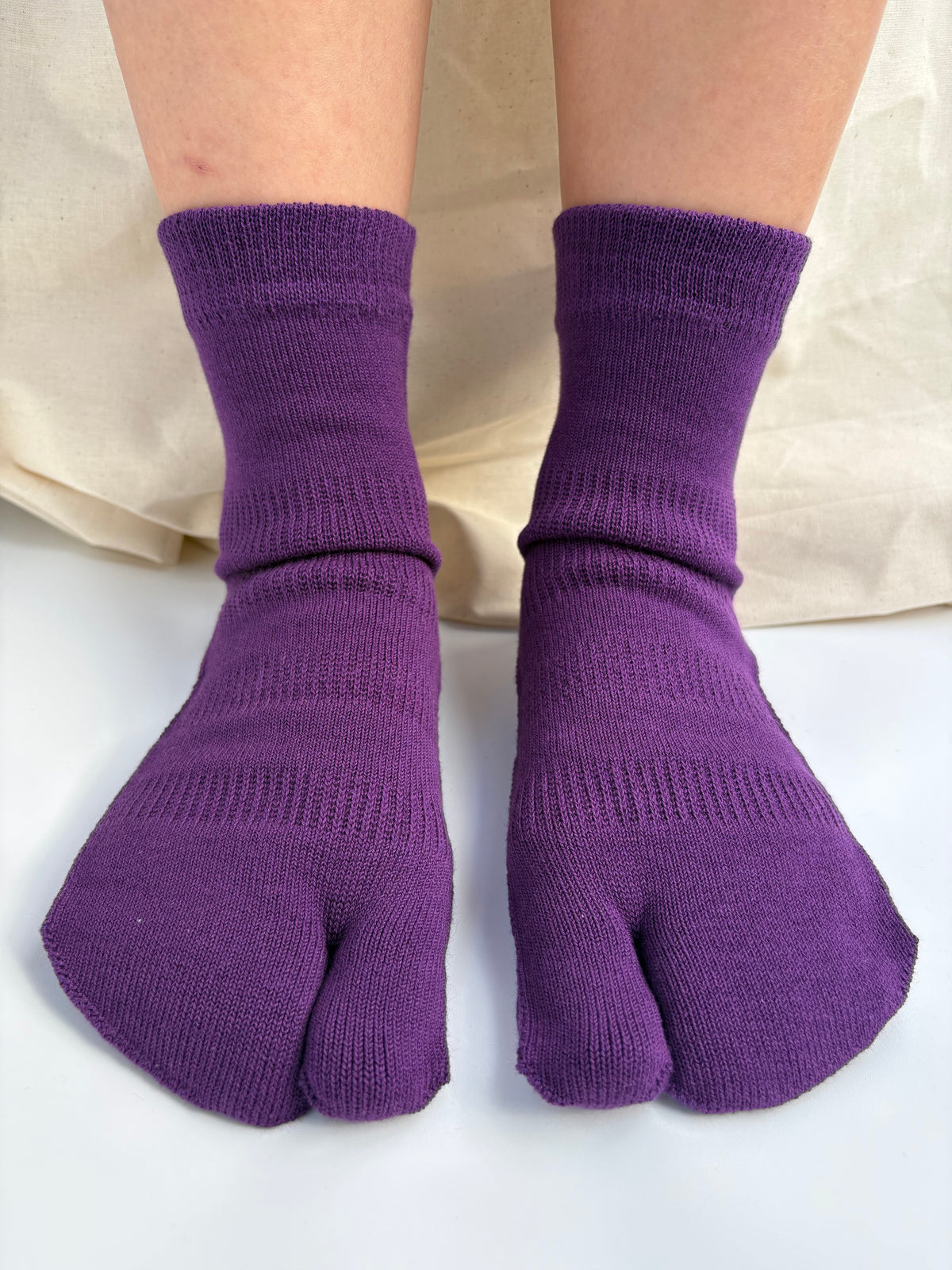 Purple ribbed tabi socks worn on a person's feet, shown against a light neutral fabric backdrop.
