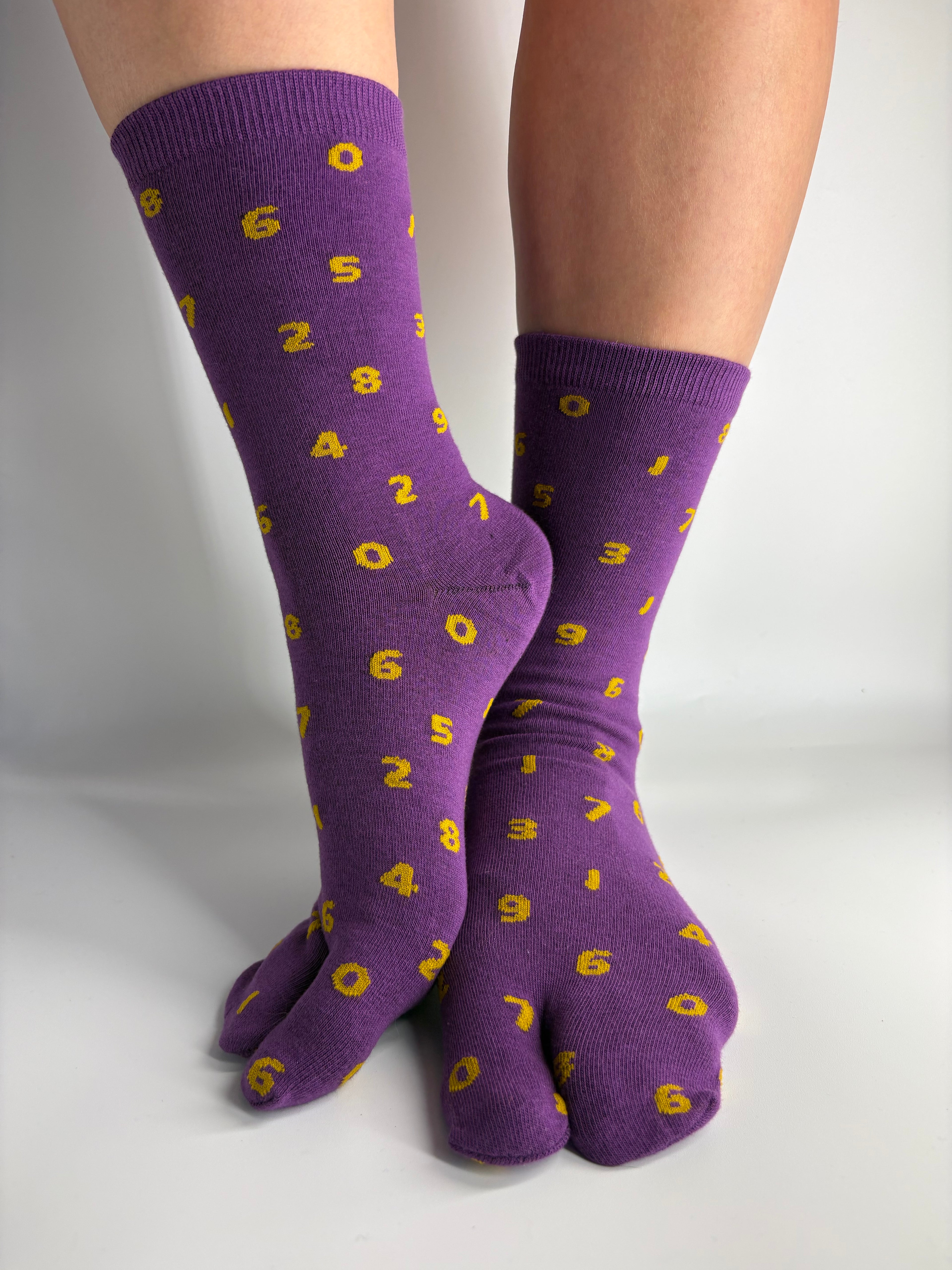 Purple split-sole socks with a yellow pattern of orange digital numbers as a print, shown on feet against a plain white background.