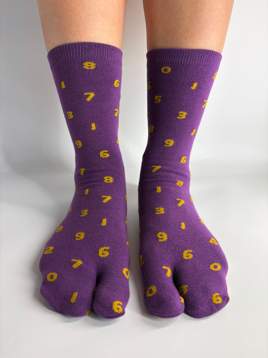 Purple split-sole socks with a yellow pattern of orange umbers as a print, shown on feet against a plain white background.