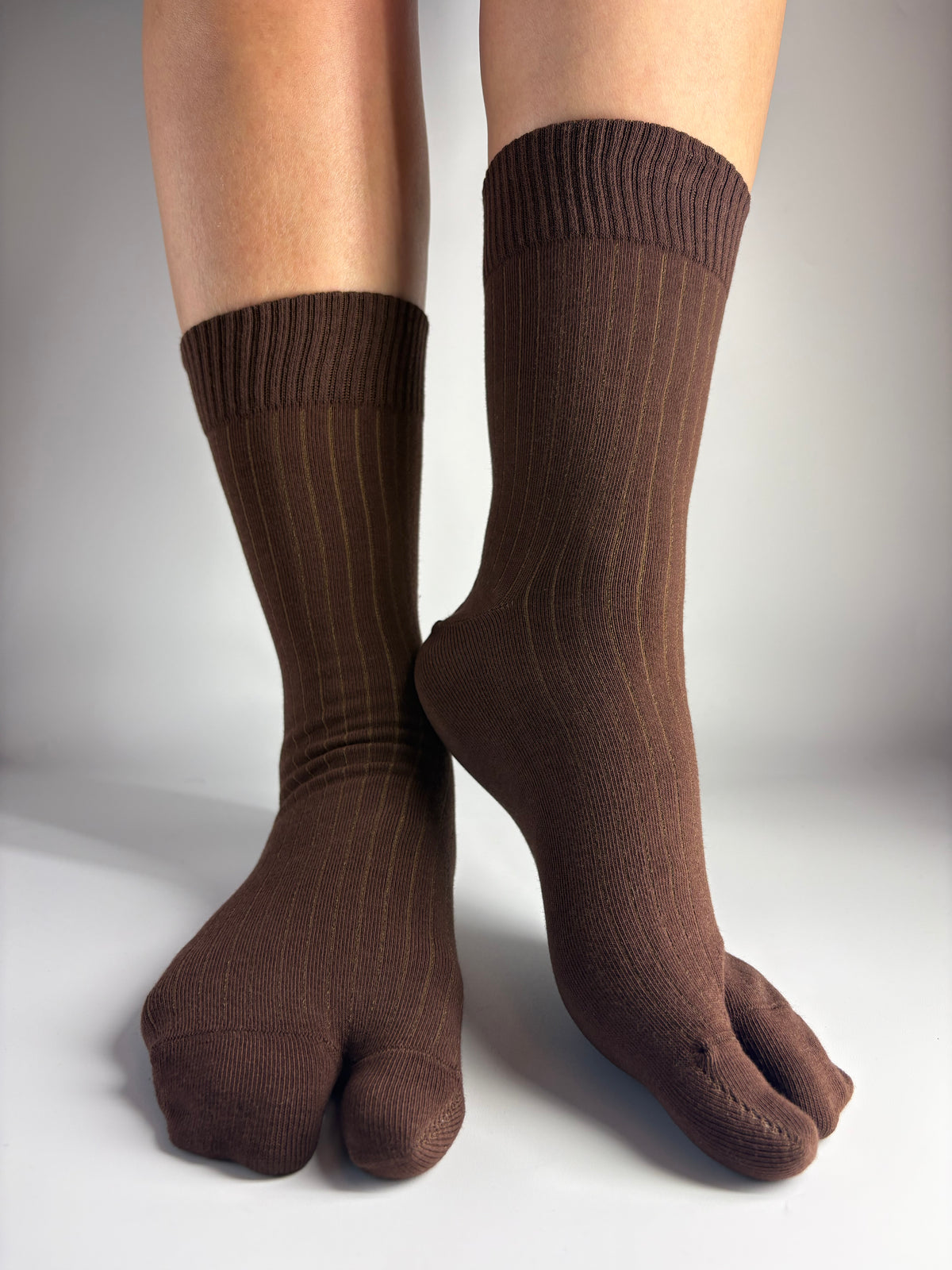 A pair of dark brown ribbed split toe socks worn on feet, shown against a plain light gray background.