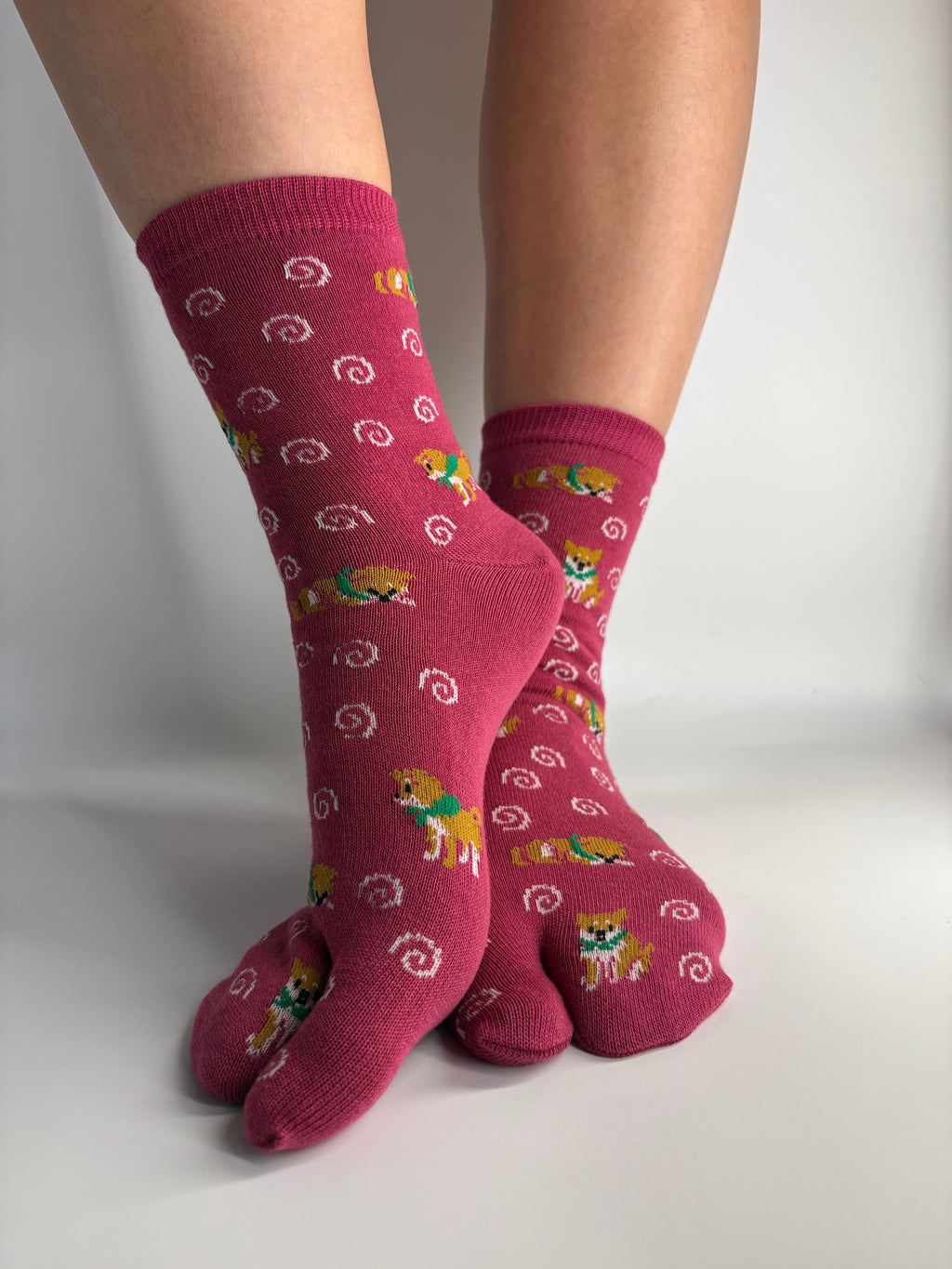 A pair of red tabi socks with a pattern of white swirls and shiba inu dog print, worn on feet against a plain white background.