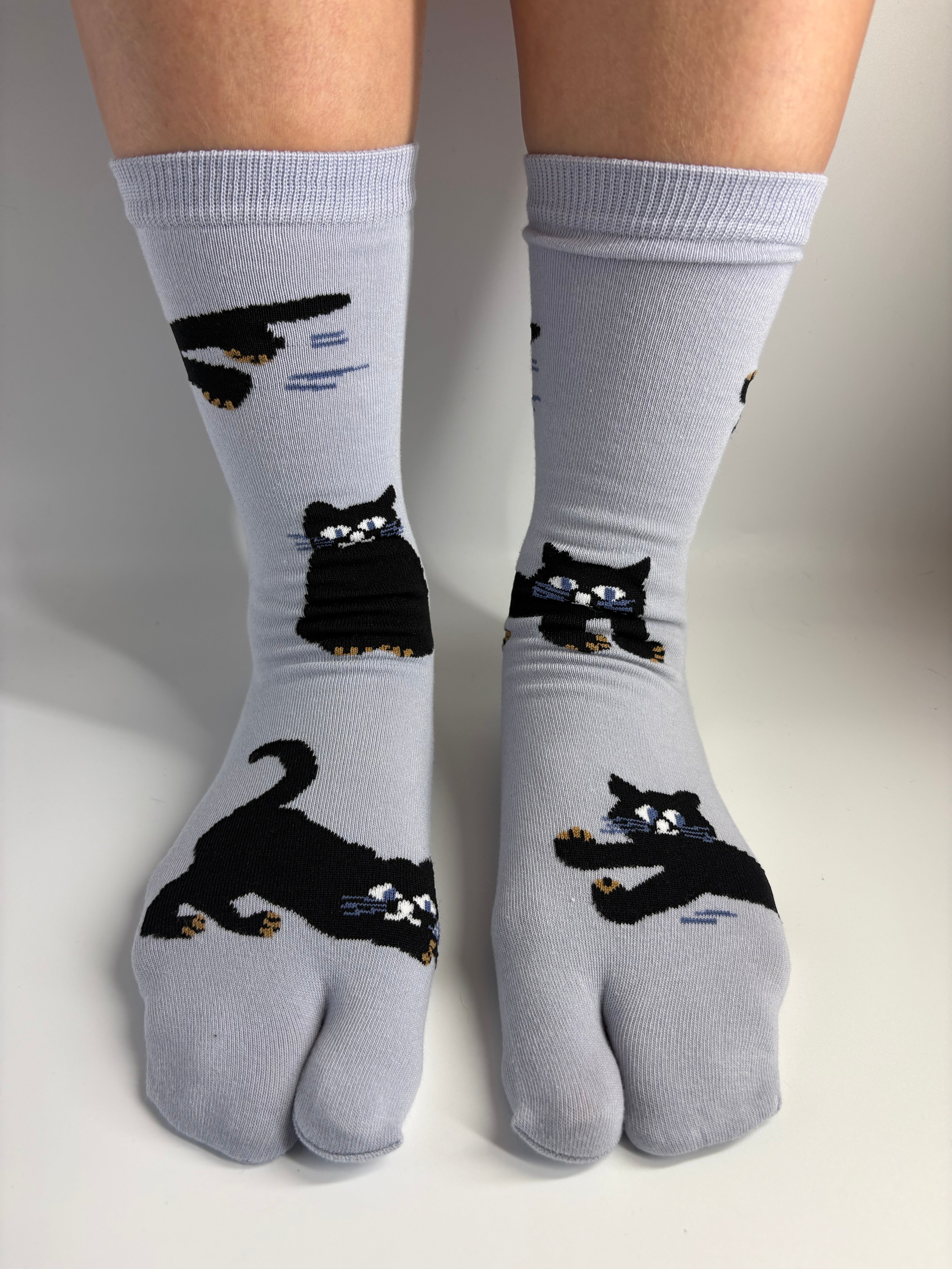 A pair of slate tab socks with black cat illustrations, worn on a person's feet against a plain light background.