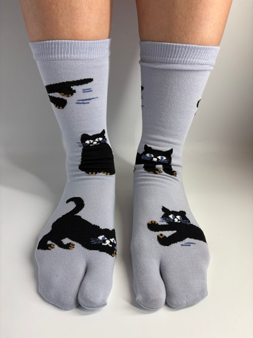 A pair of slate tab socks with black cat illustrations, worn on a person's feet against a plain light background.