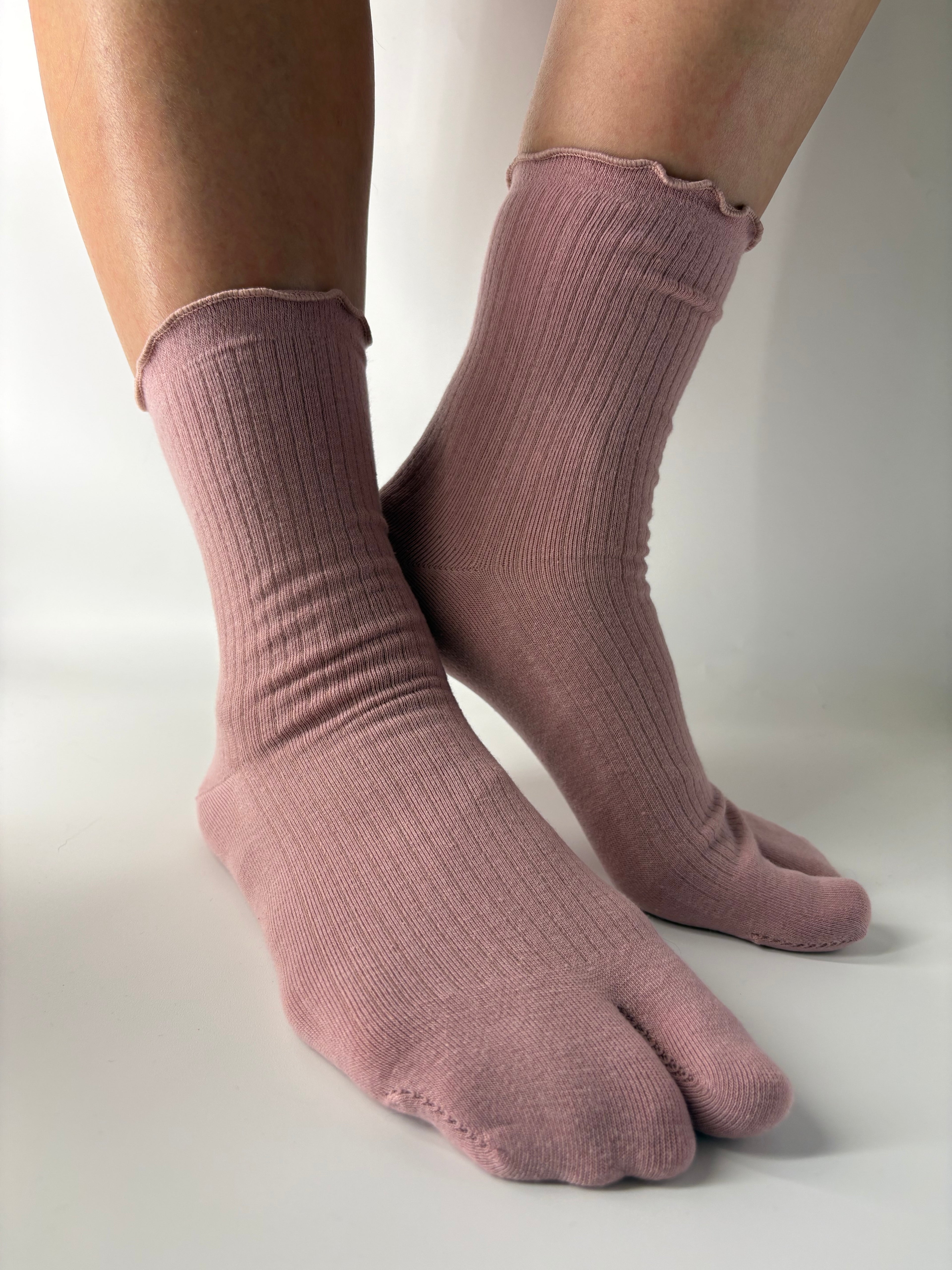 A pair of ribbed, split toe socks in a dusty mauve-pink color, shown worn on a person's feet against a clean white studio background.