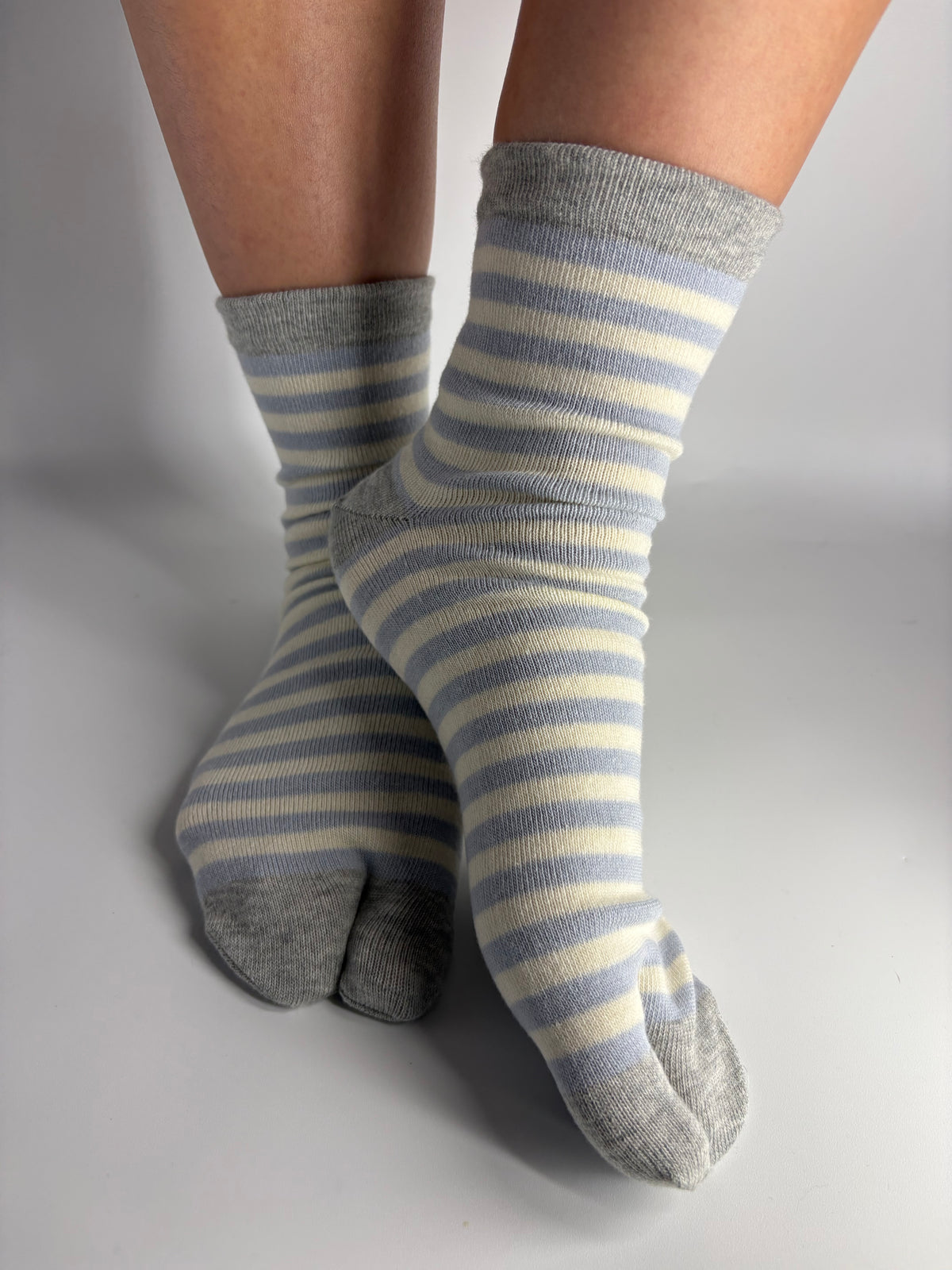A pair of gray and cream striped toe socks worn on feet, shown against a neutral gray studio background.