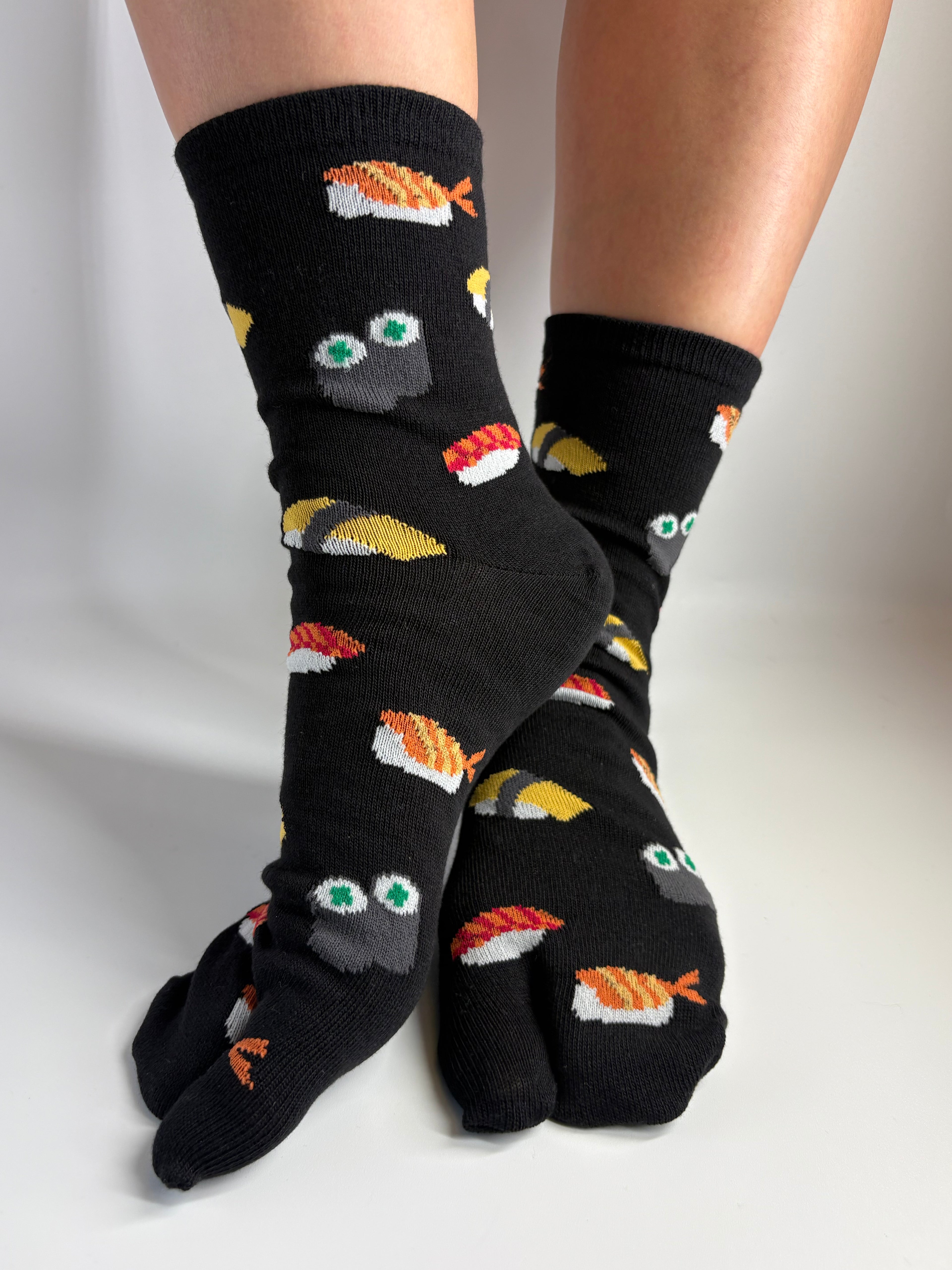 black sushi tabi socks being worn on a person's feet standing and posing on a white background