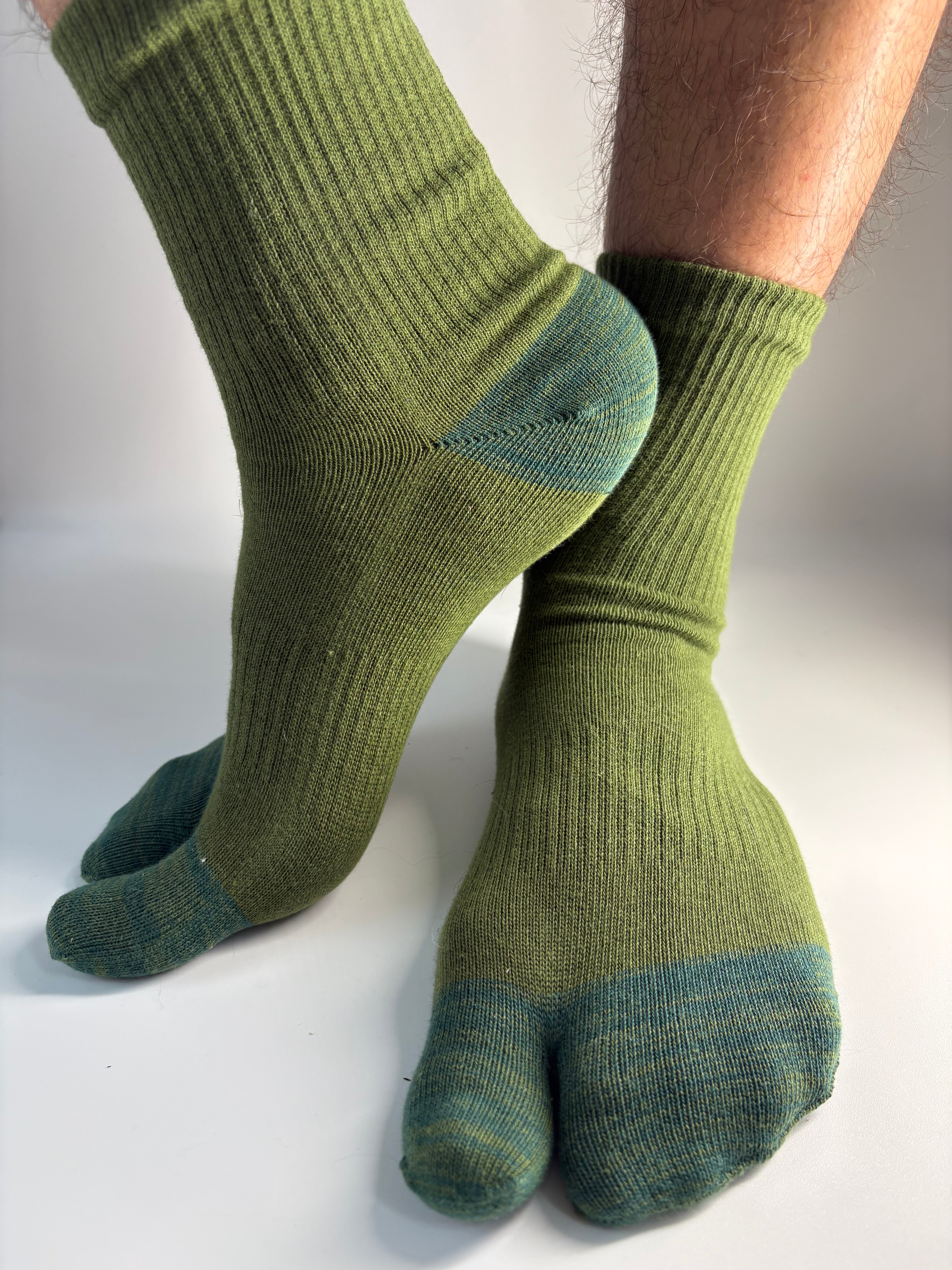 A pair of ribbed green tabi split toe socks worn on feet, shown against a plain light background.