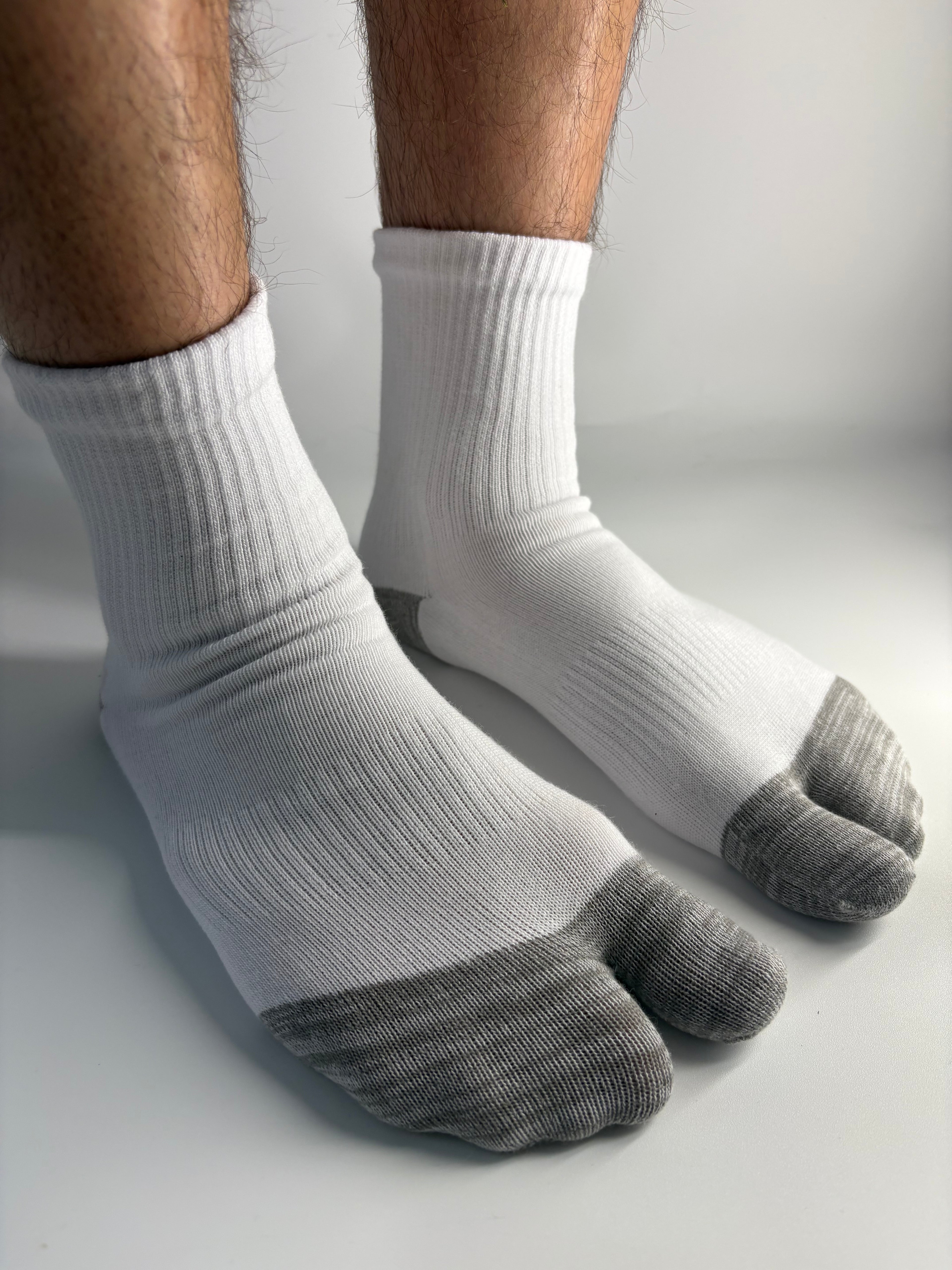A pair of white ribbed socks with gray toe sections worn on a person's feet, shown against a plain light gray background.