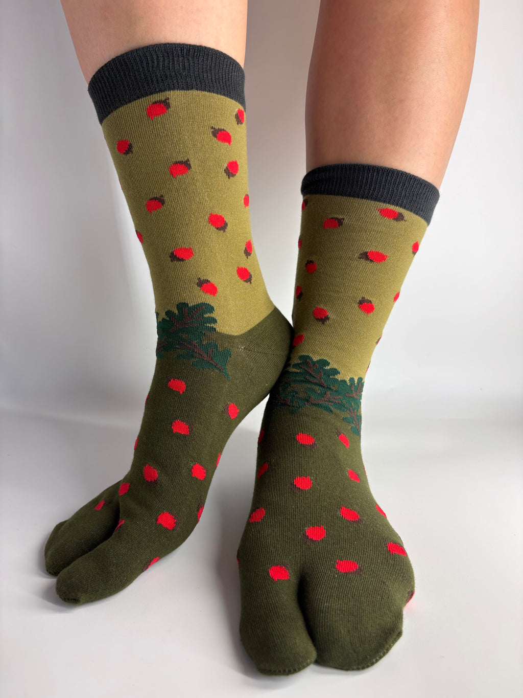 A pair of olive green tab socks with red vegetable motifs and dark green tree designs, worn on feet against a light gray background.